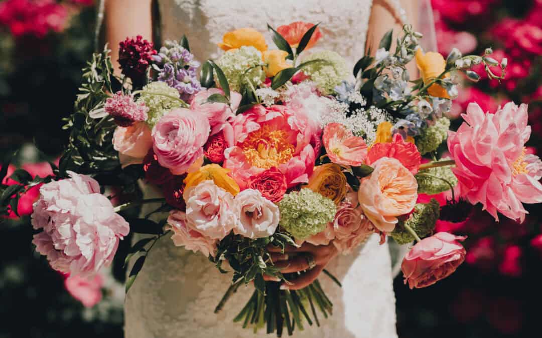 A bride holding a colorful bouquet in front of a garden